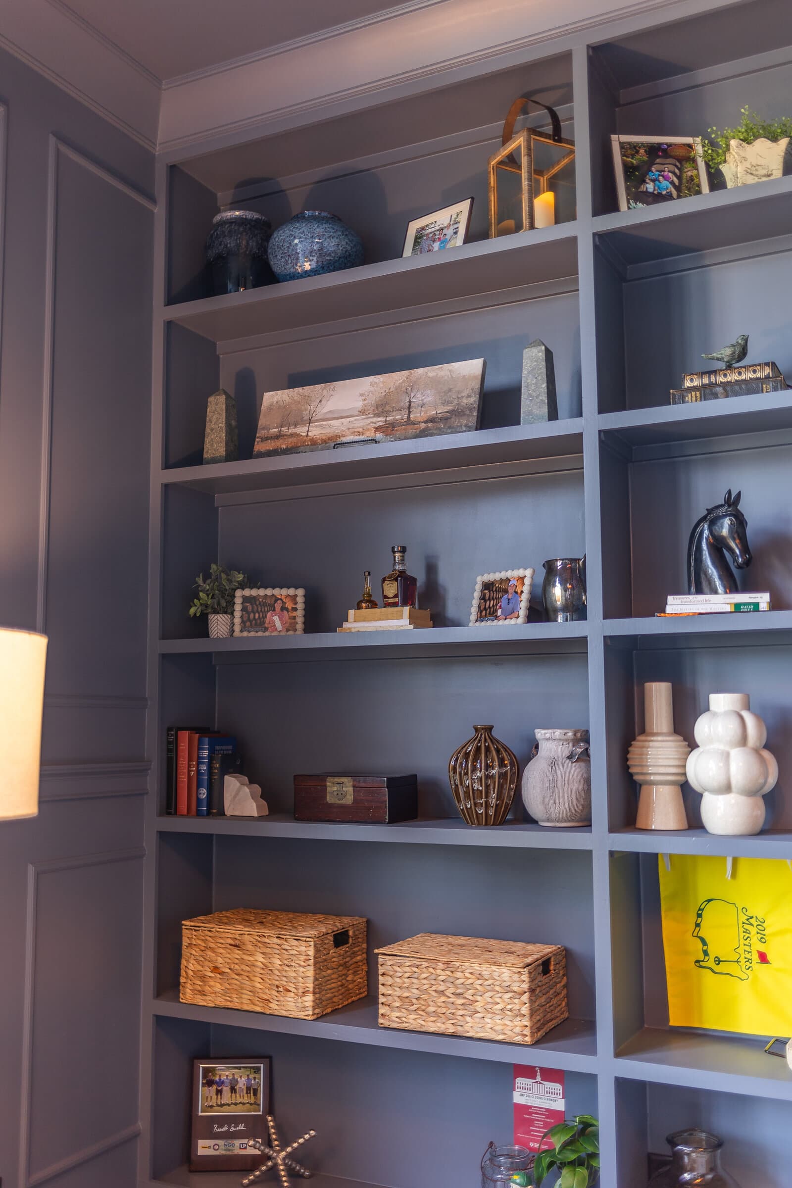 Floor to ceiling built-in shelving painted soft blue-grey, styled with antique books, ceramics, framed art and woven baskets