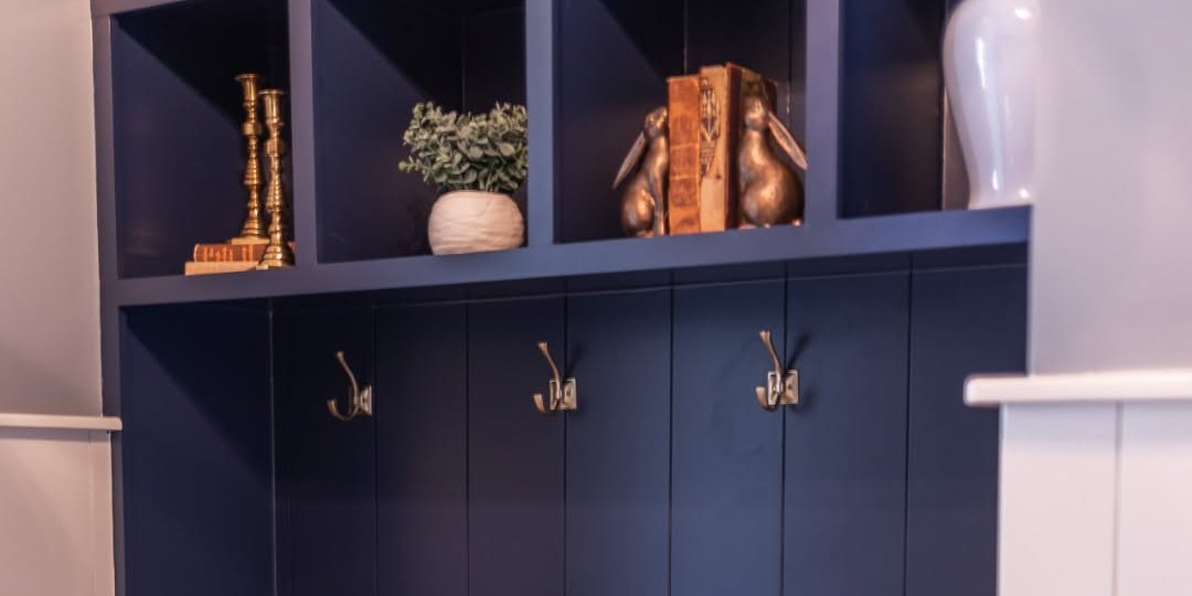 Navy mudroom lockers with brass hooks, and open cubbies above holding candlesticks, books and rabbit bookends